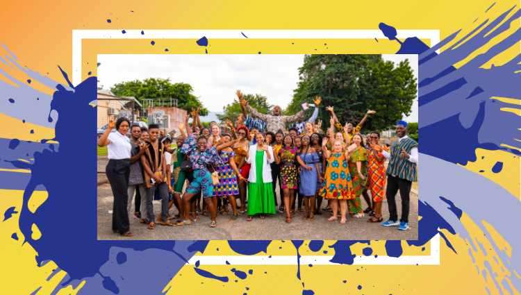 A group of people, some dressed in African patterns, raise their arms and smile while standing outside in Ghana